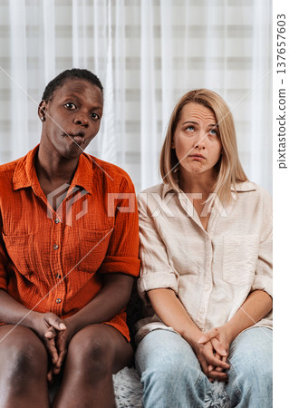 Two bored women making funny faces while sitting on the couch Two bored women making funny faces while sitting on the couch 137657603