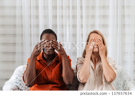 Two diverse women covering their eyes with their hands 137657634