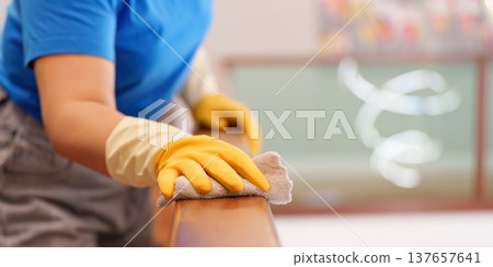 Housekeeping. Woman cleaning a wooden railing with a cloth. Housekeeping. Woman cleaning a wooden railing with a cloth. 137657641