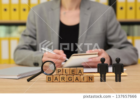 Legal professional discussing plea bargain with wooden blocks and figurines on a desk in a law office full of yellow files 137657666