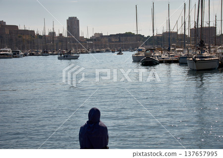 Woman wearing a hijab observes the boats and the horizon from the dock in Marseille, surrounded by water and masts on a sunny day 137657995