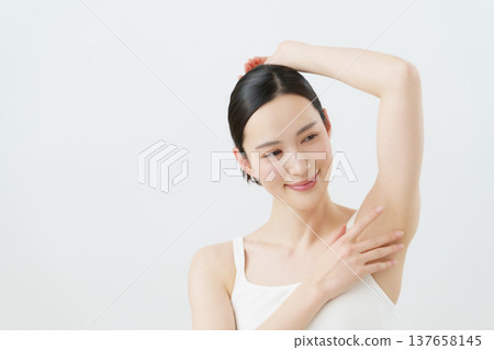 A young Japanese woman smiles with her hand on her side against a white background; hair removal image. 137658145