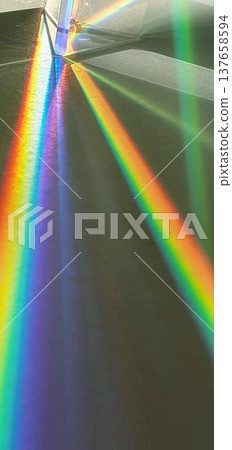 Phone photo of a triangular prism in sunlight creating rainbow lines. Abstract light scene showing color dispersion, geometry, and playful visual effects. 137658594
