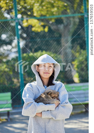 在一個陽光明媚的春日，一位少女在公園裡和一隻可愛的博美幼犬玩耍。 137659503