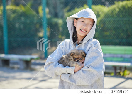 在一個陽光明媚的春日，一位少女在公園裡和一隻可愛的博美幼犬玩耍。 137659505