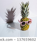 Pineapple wearing pink sunglasses stands on a glass surface casting a shadow in bright light 137659602