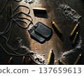 Military dog tags and spent bullet shells are arranged on a metal surface with traces of powder visible in the setting 137659613