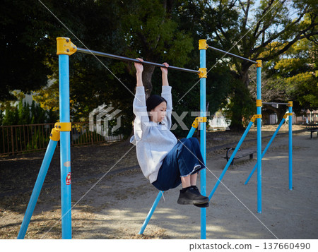 春日午後，一位十幾歲的女孩在公園的單槓上快樂地玩耍。 137660490
