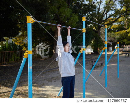 春日午後，一位十幾歲的女孩在公園的單槓上快樂地玩耍。 137660787