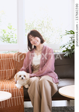 一位日本女性和她的馬爾濟斯犬坐在沙發上;與寵物相伴的生活方式;在客廳裡與狗狗共度的美好生活。 一位日本女性和她的馬爾濟斯犬坐在沙發上;與寵物相伴的生活方式;在客廳裡與狗狗共度的美好生活。 137661590