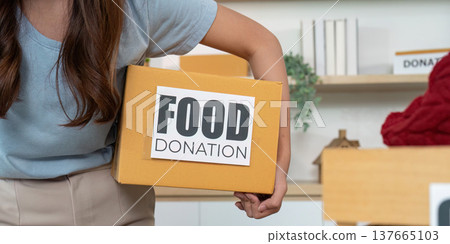 Food Donation Effort. Woman carrying a box labeled 'Food Donation' for community outreach. Food Donation Effort. Woman carrying a box labeled 'Food Donation' for community outreach. 137665103