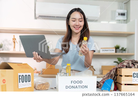 Food Donation. A woman multitasking with a laptop and food donation items. 137665164