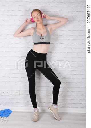 Tall, attractive redhead girl in black leggings and a grey sports bra, exercising at the gym 137665465