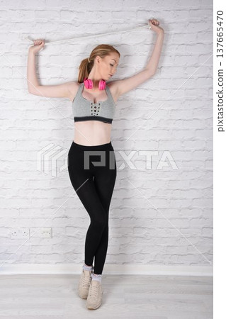 Tall, attractive redhead girl in black leggings and a grey sports bra, exercising at the gym 137665470