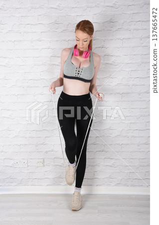 Tall, attractive redhead girl in black leggings and a grey sports bra, exercising at the gym 137665472