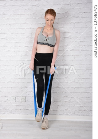 Tall, attractive redhead girl in black leggings and a grey sports bra, exercising at the gym Tall, attractive redhead girl in black leggings and a grey sports bra, exercising at the gym 137665475