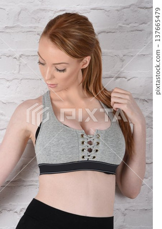 Tall, attractive redhead girl in black leggings and a grey sports bra, exercising at the gym Tall, attractive redhead girl in black leggings and a grey sports bra, exercising at the gym 137665479