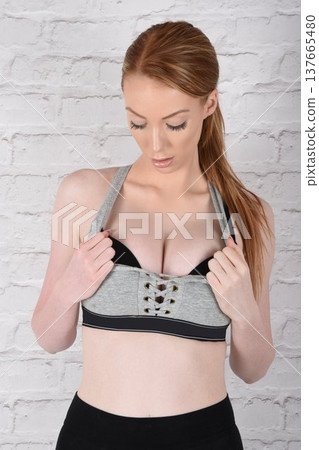 Tall, attractive redhead girl in black leggings and a grey sports bra, exercising at the gym 137665480