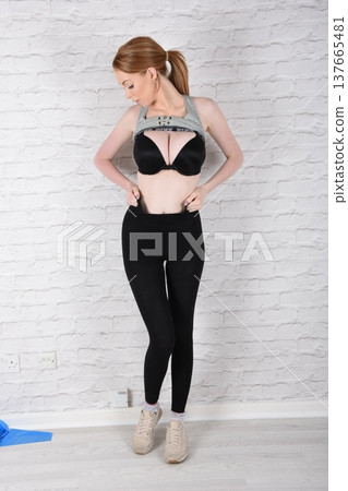 Tall, attractive redhead girl in black leggings and a grey sports bra, exercising at the gym Tall, attractive redhead girl in black leggings and a grey sports bra, exercising at the gym 137665481