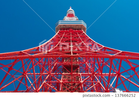 Tokyo Tower, standing out against the deep blue sky during the daytime, is a vibrant red and white landmark that symbolizes Japan's capital city. 137666252
