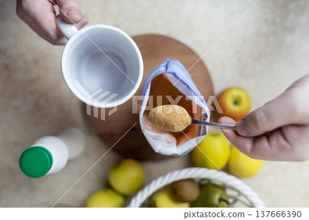 Person adding apple fiber powder to a glass of yogurt, surrounded by fresh apples and walnuts. Healthy prebiotic supplement for gut health, digestion and weight management. Person adding apple fiber powder to a glass of yogurt, surrounded by fresh apples and walnuts. Healthy prebiotic supplement for gut health, digestion and weight management. 137666390