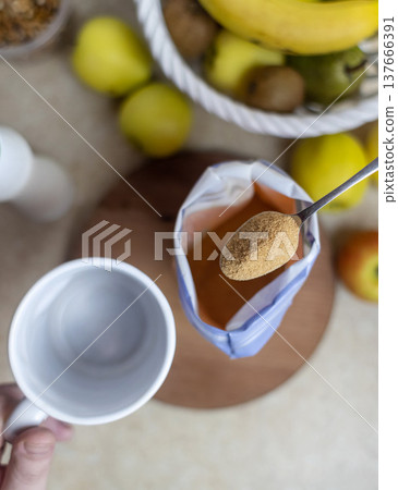 Person adding apple fiber powder to a glass of yogurt, surrounded by fresh apples and walnuts. Healthy prebiotic supplement for gut health, digestion and weight management. 137666391