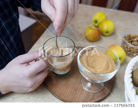 Person adding apple fiber powder to a glass of yogurt, surrounded by fresh apples and walnuts. Healthy prebiotic supplement for gut health, digestion and weight management. 137666393