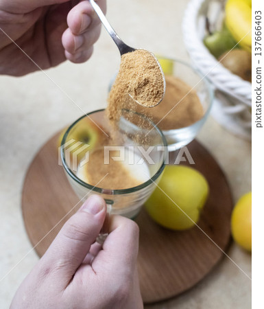 Person adding apple fiber powder to a glass of yogurt, surrounded by fresh apples and walnuts. Healthy prebiotic supplement for gut health, digestion and weight management. 137666403