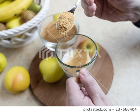 Person adding apple fiber powder to a glass of yogurt, surrounded by fresh apples and walnuts. Healthy prebiotic supplement for gut health, digestion and weight management. Person adding apple fiber powder to a glass of yogurt, surrounded by fresh apples and walnuts. Healthy prebiotic supplement for gut health, digestion and weight management. 137666404