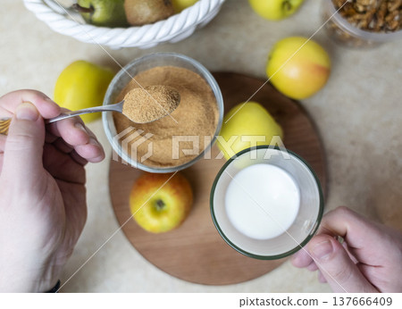 Person adding apple fiber powder to a glass of yogurt, surrounded by fresh apples and walnuts. Healthy prebiotic supplement for gut health, digestion and weight management. 137666409