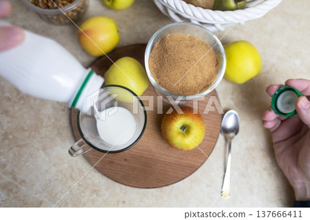 Person adding apple fiber powder to a glass of yogurt, surrounded by fresh apples and walnuts. Healthy prebiotic supplement for gut health, digestion and weight management. Person adding apple fiber powder to a glass of yogurt, surrounded by fresh apples and walnuts. Healthy prebiotic supplement for gut health, digestion and weight management. 137666411