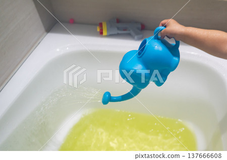 A child playing with an elephant-shaped watering can in the bath. 137666608