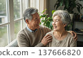 Happy Asian senior couple embracing and smiling together by window with houseplants in cozy home interior wearing beige sweaters 137666820