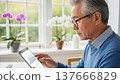 Senior Asian businessman analyzing financial data charts graphs on tablet device at bright home office window 137666829