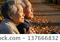 Senior Asian couple sitting together outdoors in warm sunlight holding hands with peaceful expressions during golden hour autumn afternoon 137666832