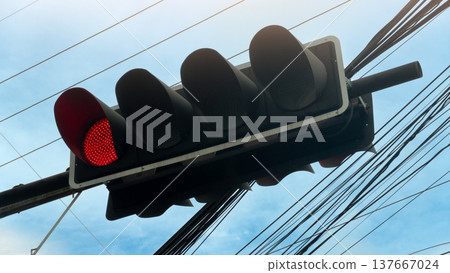 South view of a traffic light panel with a red light attached. Signs on the front and back side by side. Background consists of a tangled network of traffic lights. Under the sky. South view of a traffic light panel with a red light attached. Signs on the front and back side by side. Background consists of a tangled network of traffic lights. Under the sky. 137667024