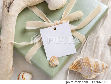 Blank square gift tag mockup on sage green present near seashells. Product label design Blank square gift tag mockup on sage green present near seashells. Product label design 137667086