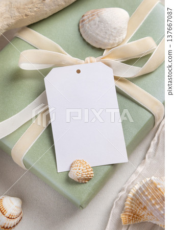 Blank gift tag mockup on light green present with a ribbon bow near seashells. Coastal packaging Blank gift tag mockup on light green present with a ribbon bow near seashells. Coastal packaging 137667087