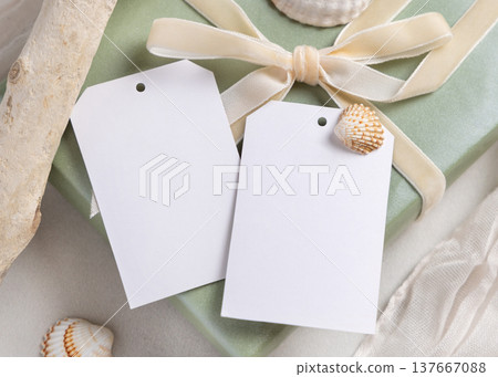 Vertical gift tags mockup on sage green present with a ribbon bow near seashells. Summer packaging Vertical gift tags mockup on sage green present with a ribbon bow near seashells. Summer packaging 137667088