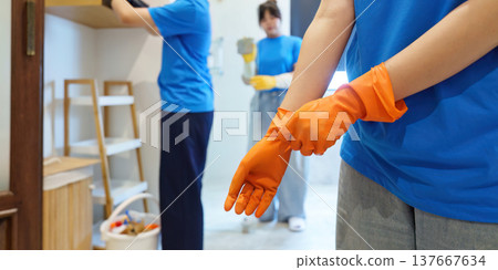 Preparation for Cleaning. Woman putting on orange gloves before cleaning. 137667634