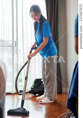 Home Cleaning. Young woman vacuuming the floor in a bright living room. Home Cleaning. Young woman vacuuming the floor in a bright living room. 137667635