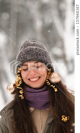 A beautiful young woman in winter clothes is happily spending her free time in a snowy forest. She enjoys the first snow. Active winter recreation. A beautiful young woman in winter clothes is happily spending her free time in a snowy forest. She enjoys the first snow. Active winter recreation. 137668167
