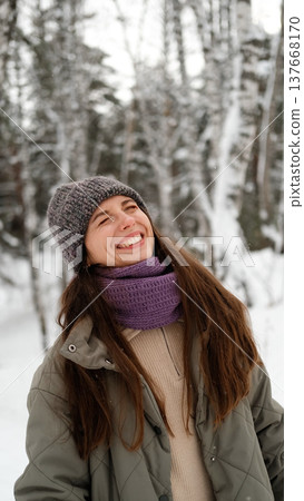 A beautiful young woman in winter clothes is happily spending her free time in a snowy forest. She enjoys the first snow. Active winter recreation. 137668170