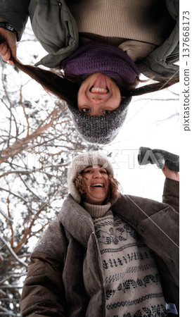 Two cheerful female friends are having fun and laughing in a winter park. The camera is facing upwards. 137668173