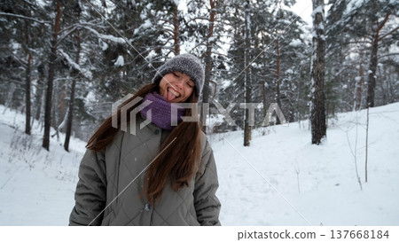 A beautiful young woman in winter clothes is happily spending her free time in a snowy forest. She enjoys the first snow. Active winter recreation. 137668184