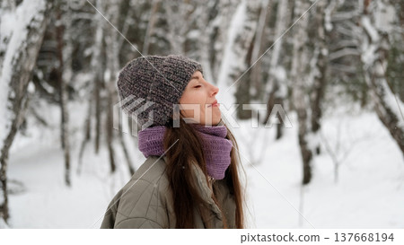 A beautiful young woman in winter clothes is happily spending her free time in a snowy forest. She enjoys the first snow. Active winter recreation. 137668194