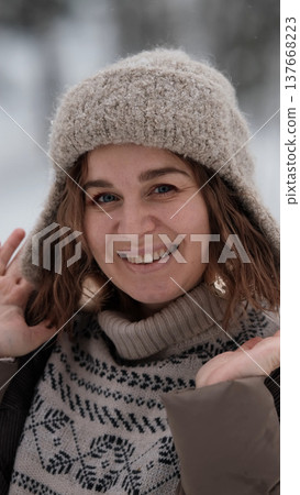 A beautiful woman in winter clothing enjoys her free time in a snowy forest. Portrait of a woman enjoying the first snow. Active winter recreation. 137668223