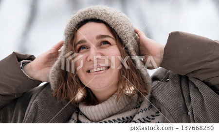 A beautiful woman in winter clothing enjoys her free time in a snowy forest. Portrait of a woman enjoying the first snow. Active winter recreation. 137668230