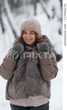 A beautiful woman in winter clothing enjoys her free time in a snowy forest. Portrait of a woman enjoying the first snow. Active winter recreation. A beautiful woman in winter clothing enjoys her free time in a snowy forest. Portrait of a woman enjoying the first snow. Active winter recreation. 137668236
