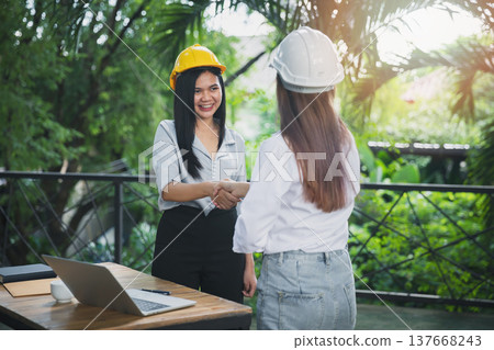 Two asian female architect and engineer in protective helmets shaking hands after meeting. Success collaboration concept. Two asian female architect and engineer in protective helmets shaking hands after meeting. Success collaboration concept. 137668243